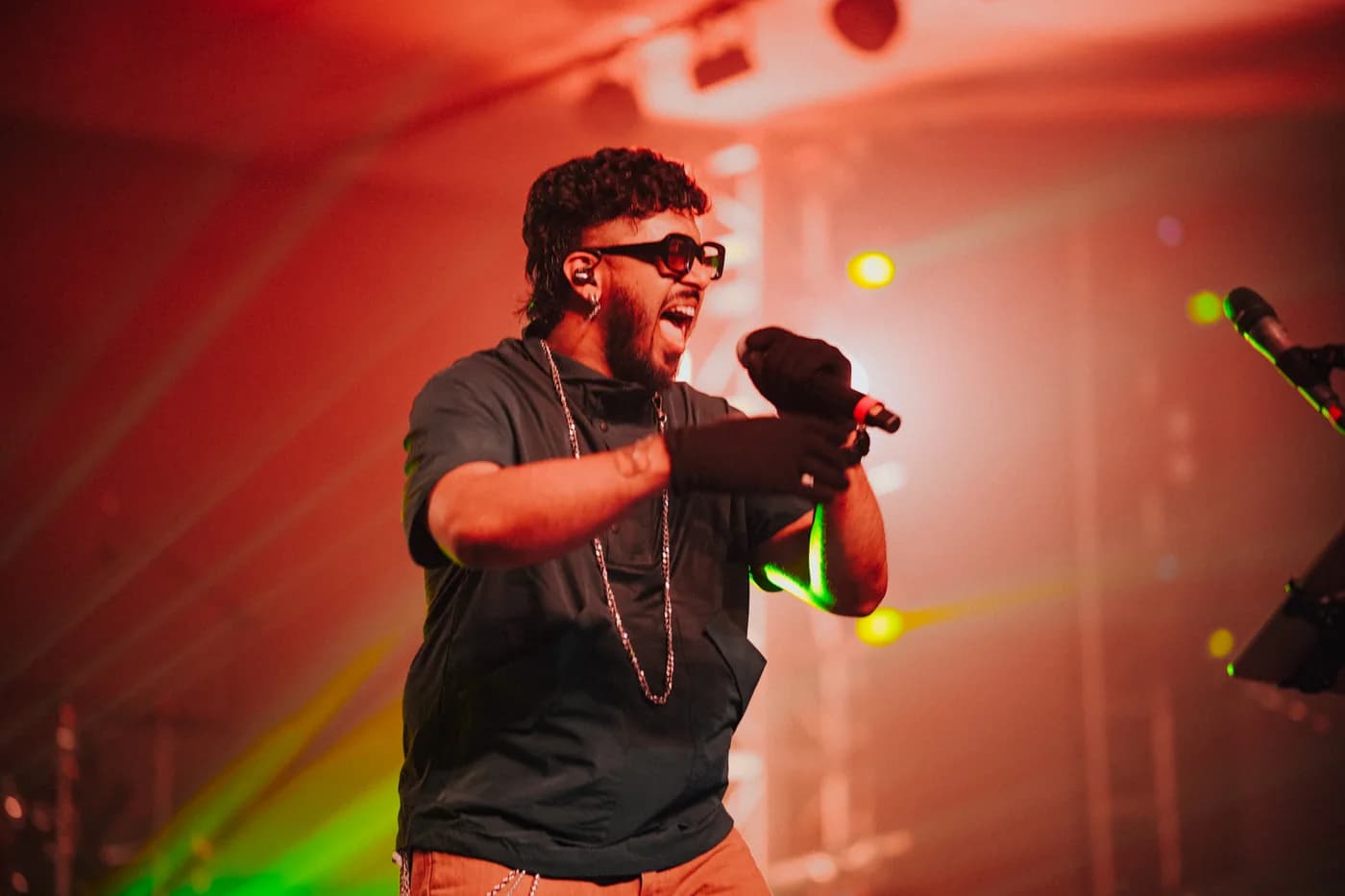 Faisal Razi singing into a microphone beneath red concert lights