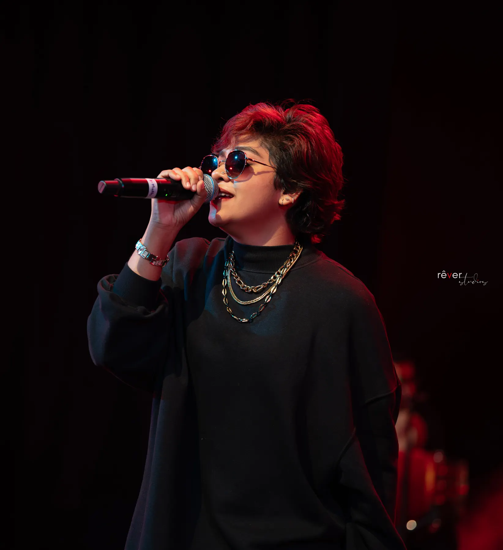 Shikha Prabhakaran singing into a microphone under warm stage lighting